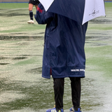 Person wearing a navy raincoat and holding a matching umbrella on a wet field.
