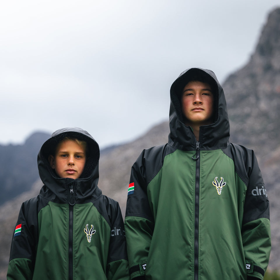 Two people wearing green and black jackets with a mountainous background